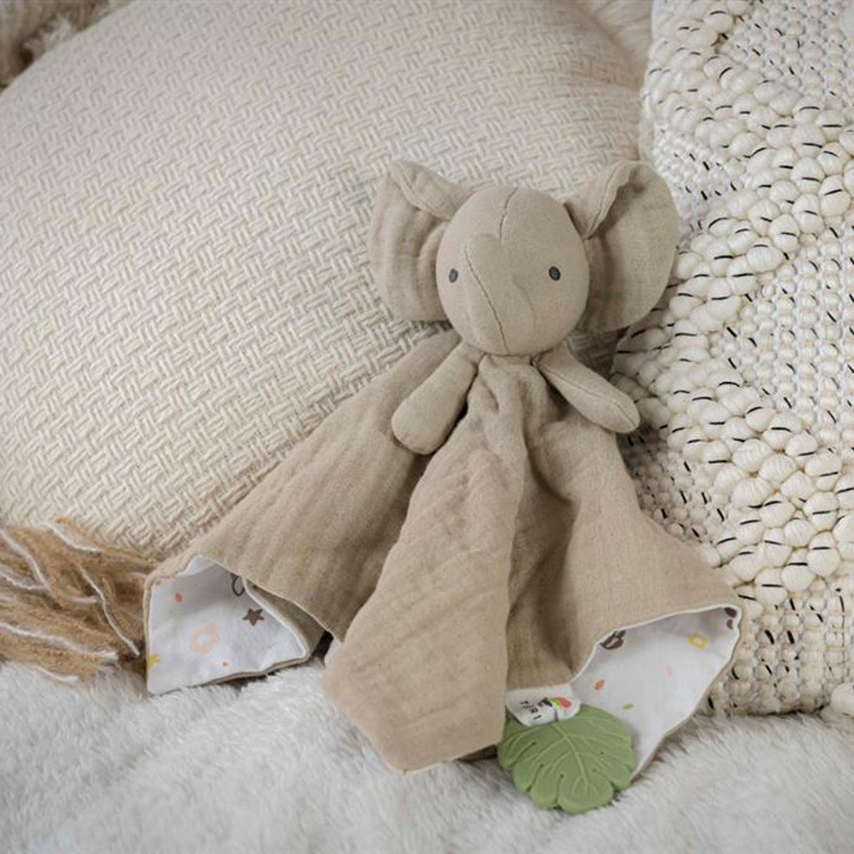 Baby muslin comforter with attached elephant toy and green leaf teether on a bed