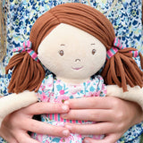 Soft rag doll with brown hair in pigtails wearing a floral dress being held by a child