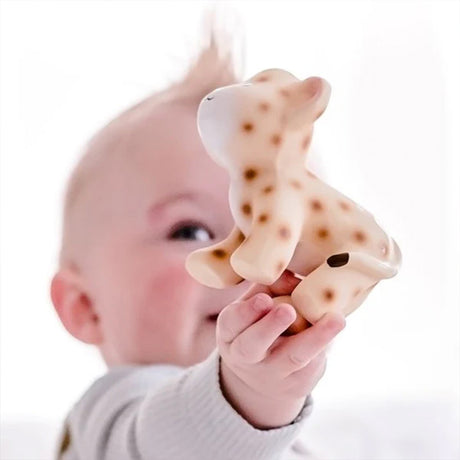 Baby holding a textured leopard teether against a white background