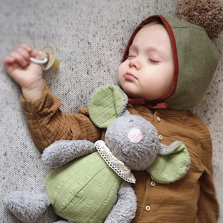Baby wearing natural colours, bonnet and brown flannel top, lying with an organic grey and green mouse soft toy