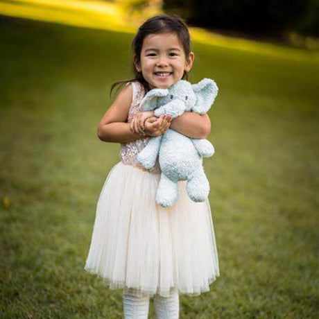 Young girl in white dress holding a stuffed organic blue elephant toy outdoors on grass