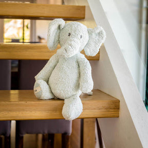 Plush organic grey blue elephant Soft toy on a wooden staircase with a blurred indoor background