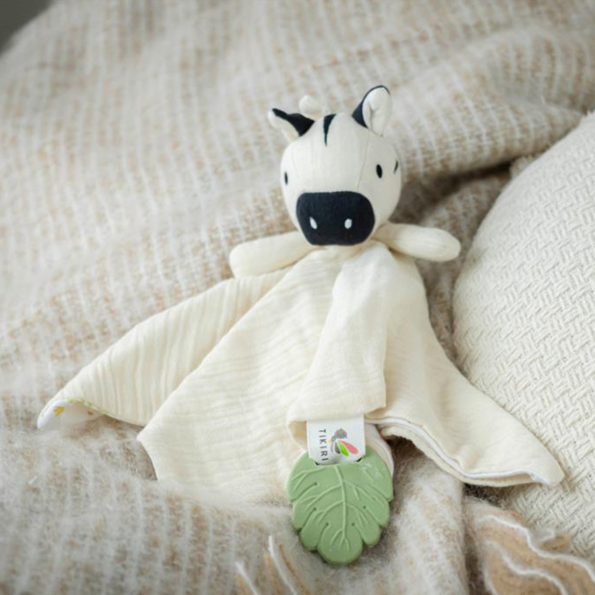 A baby muslin comforter with an attached zebra toy and green leaf teether