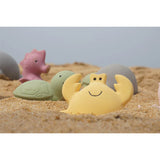 Colourful rubber bath and beach toys on a sandy surface with a clear sky.