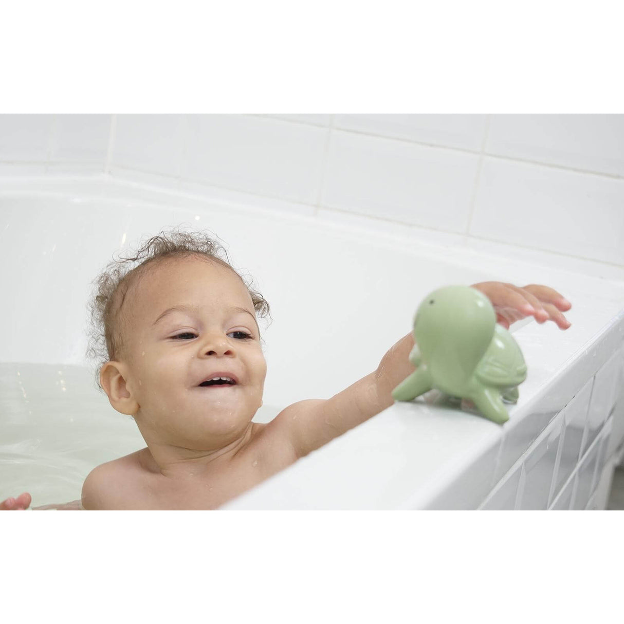 Baby playing with a green rubber turtle bath toy in a bathtub