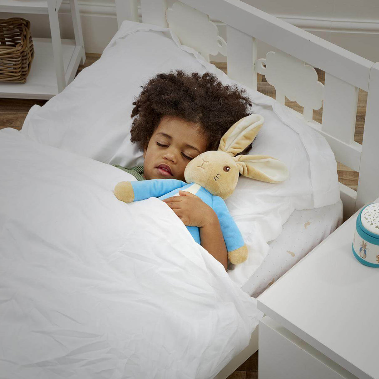 Child sleeping in a crib with a plush Peter Rabbit toy, surrounded by white bedding and a nightlight.