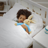 Child sleeping in a crib with a plush Peter Rabbit toy, surrounded by white bedding and a nightlight.