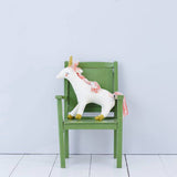 Meri Meri white unicorn soft toy sitting on a green children's chair against a pale grey wall