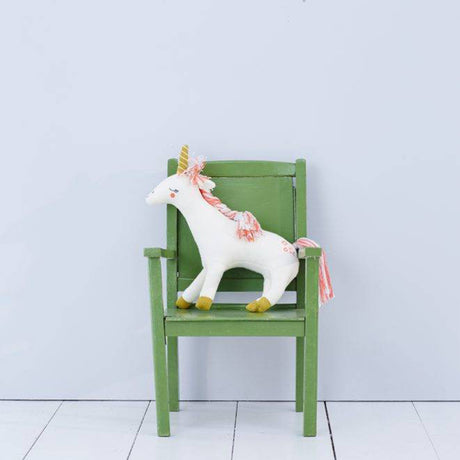 Meri Meri white unicorn soft toy sitting on a green children's chair against a pale grey wall