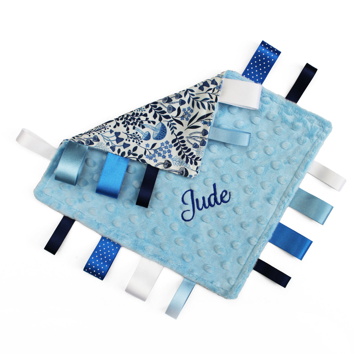 A personalized baby lovey blanket in light blue minky dot fabric with a name embroidered in navy. It features a patterned reverse side and is adorned with multiple blue, navy, white, and light blue satin ribbon tabs.