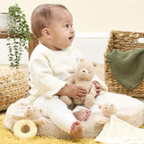 A baby sitting in a nursery setting, holding a small beige Pooh bear