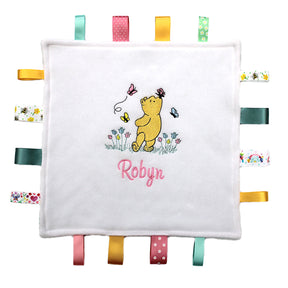 Personalised Winnie the Pooh taggy comforter with white fleece front and multiple colorful satin ribbons. 