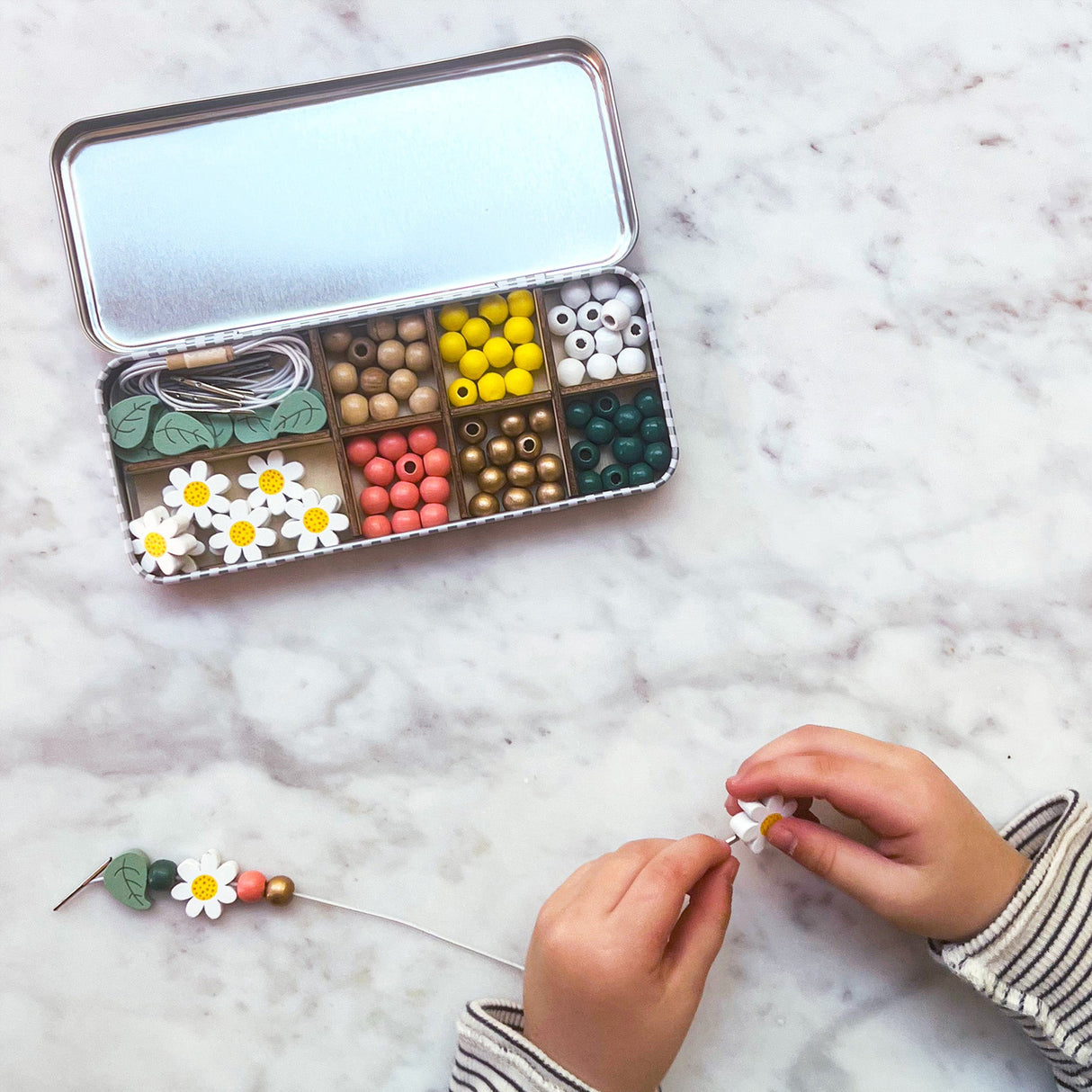 Bead kit with colourful beads and a child's hands working on a craft project on a marble surface.