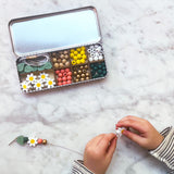 Bead kit with colourful beads and a child's hands working on a craft project on a marble surface.