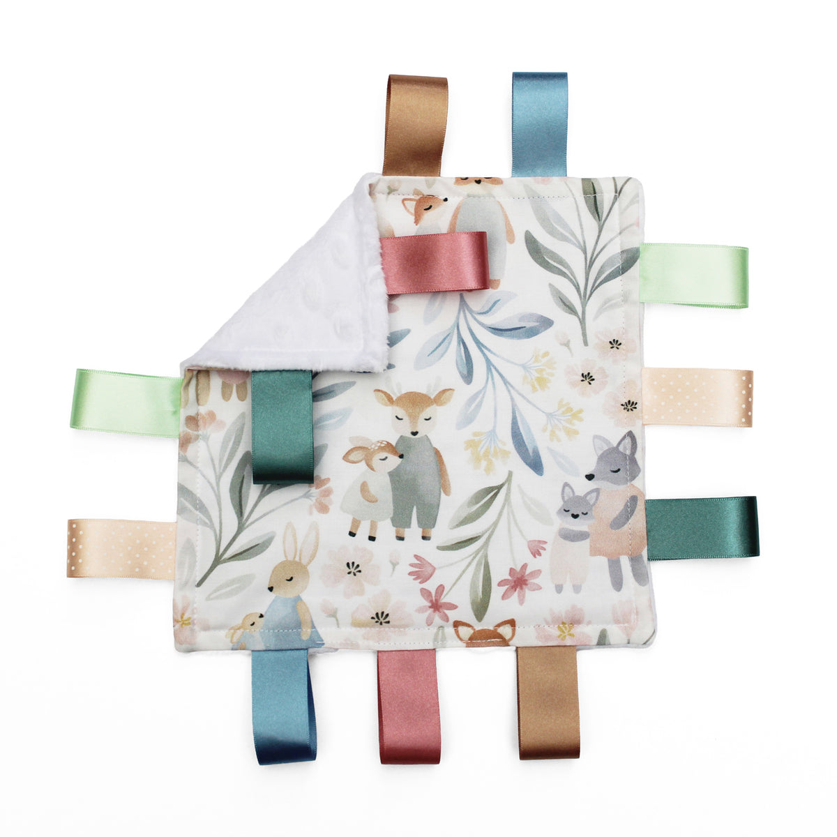 A square baby taggy comforter with a woodland animal print, featuring a white plush reverse side and colourful satin ribbon tabs in blue, green, pink, beige, and brown.