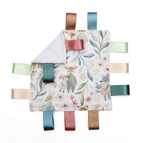 A square baby taggy comforter with a woodland animal print, featuring a white plush reverse side and colourful satin ribbon tabs in blue, green, pink, beige, and brown.