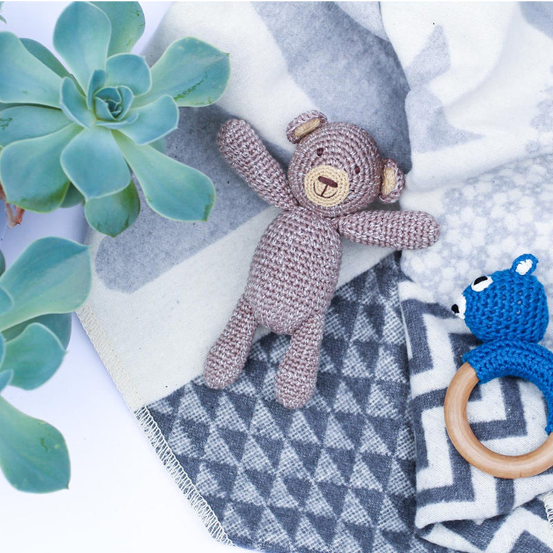 Albetta Crochet Bear Rattle in soft brown cotton, styled on a grey geometric blanket with a blue crochet teether and succulent plant