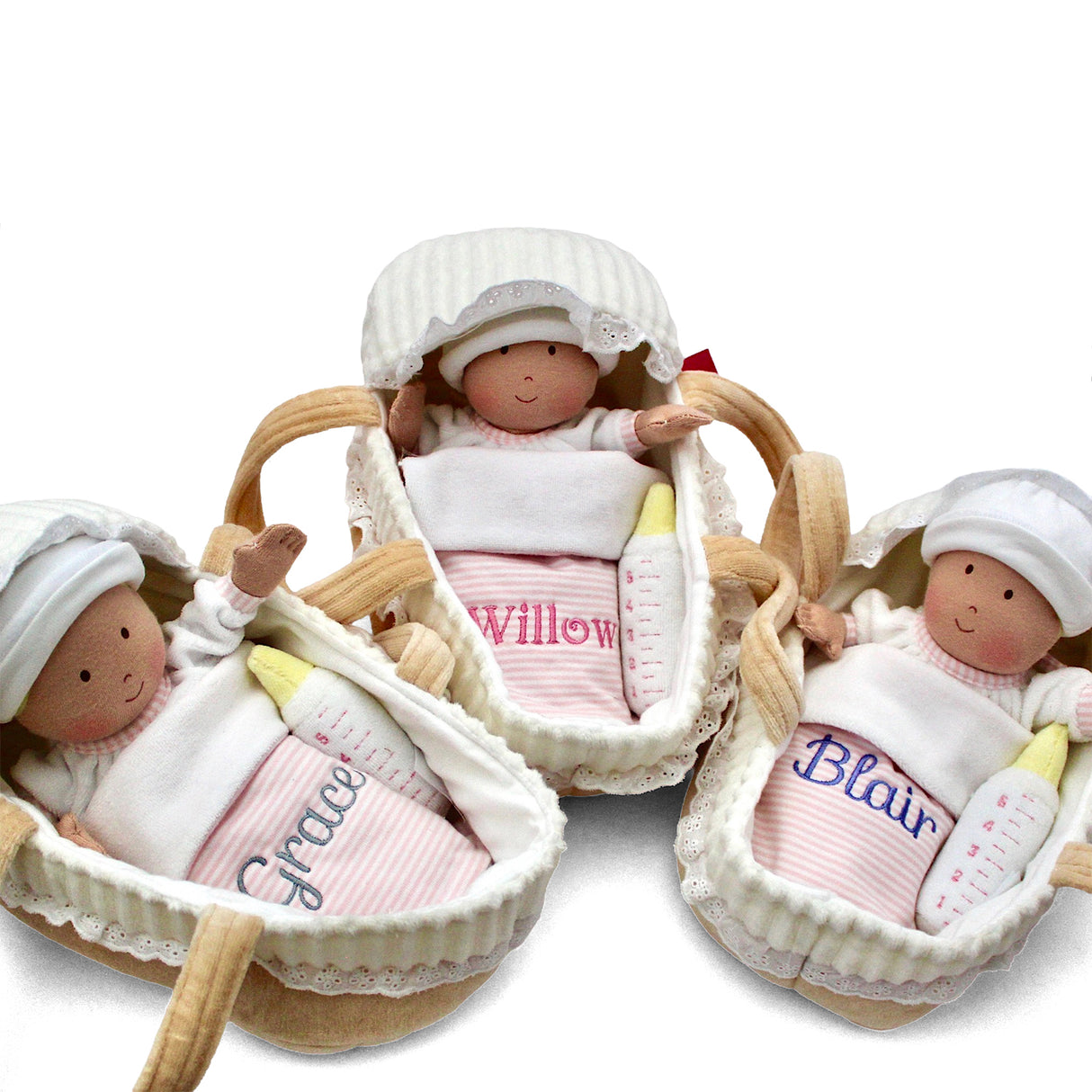 Three baby dolls in cots with names embroidered on their clothing against a white background