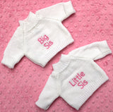 Two personalised knitted white jumpers with big sis in pink on one and little sis in pink on the other
