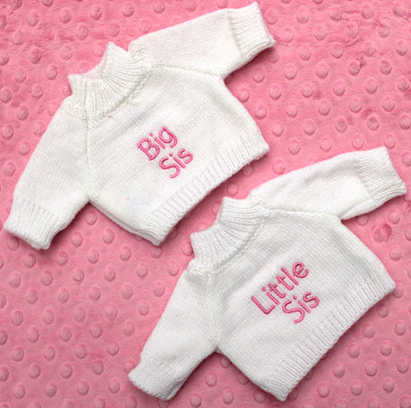 Two personalised knitted white jumpers with big sis in pink on one and little sis in pink on the other