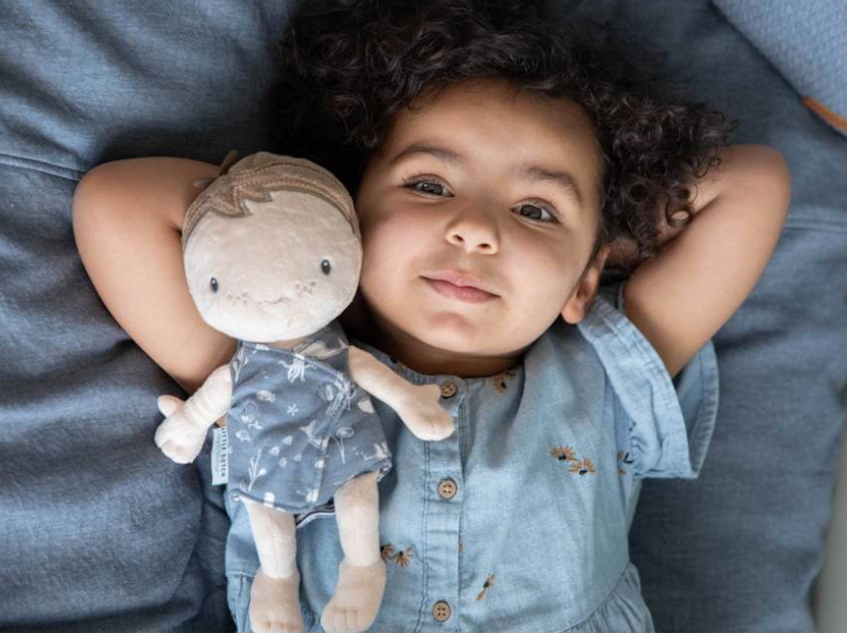 Child lying down with baby boy soft doll