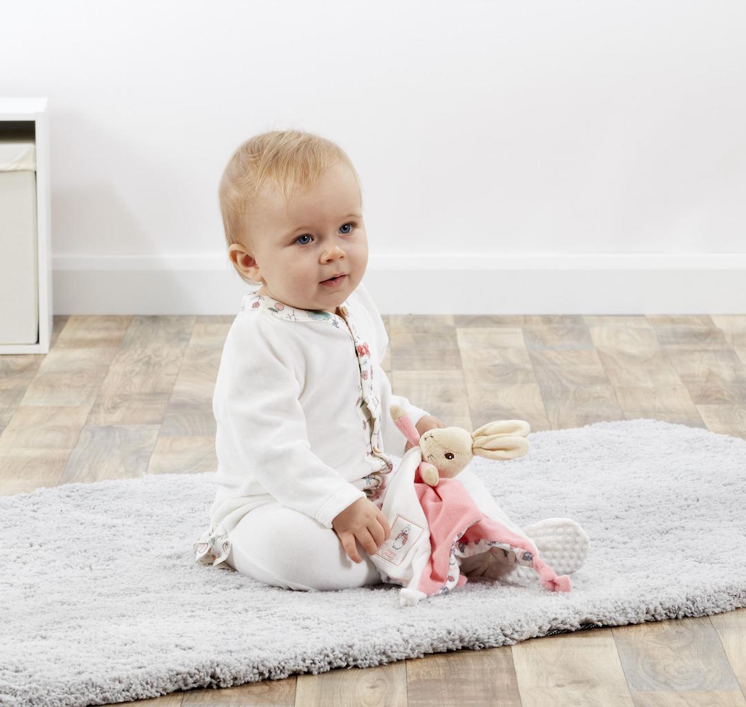 Baby holding a  white and pink Beatrix Potter Flopsy Bunny Comforter that can be personalised