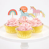 Pink-iced cupcakes in gold foil cases on a cake stand decorated with Meri Meri unicorn, rainbow and I Believe In Unicorns toppers