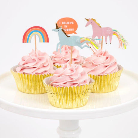 Pink-iced cupcakes in gold foil cases on a cake stand decorated with Meri Meri unicorn, rainbow and I Believe In Unicorns toppers