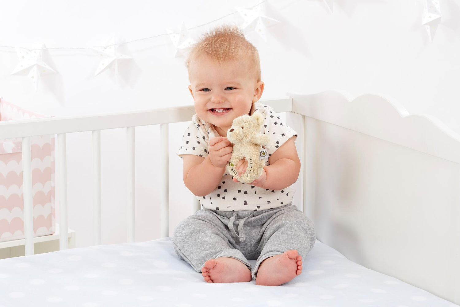 Baby holding a Winnie The Pooh Ring Rattle in a cot 