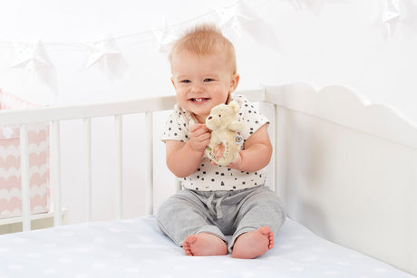 Baby holding a Winnie The Pooh Ring Rattle in a cot 