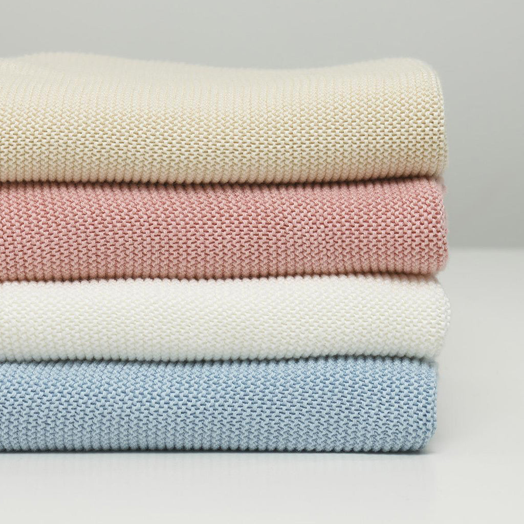 A luxurious organic baby blanket of stunning quality and a simple knit design and intricate finish shown with choice of four colours: Blossom Pink, Duck Egg Blue, Eco White or Natural