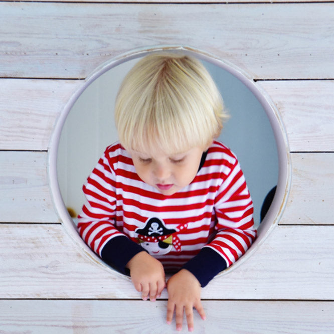 Red and white striped pirate pyjamas suit by Powell Craft worn by a young child climbing through hole in woodwork