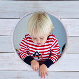 Red and white striped pirate pyjamas suit by Powell Craft worn by a young child climbing through hole in woodwork